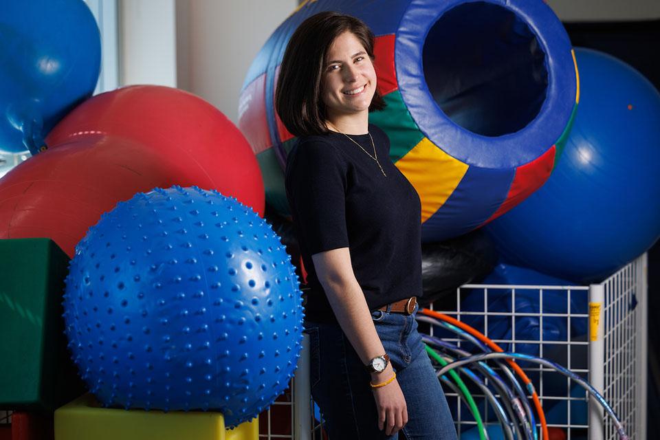 A student stands next to a collection of large inflatable balls, hula hoops and other items used in therapy.